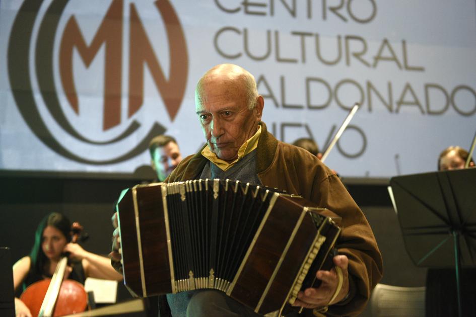 Hombre tocando el acordeón y atrás está la Orquesta Juvenil del Sodre