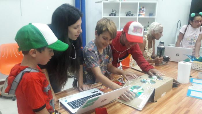 Niños y niñas junto a tallerista frente a pc