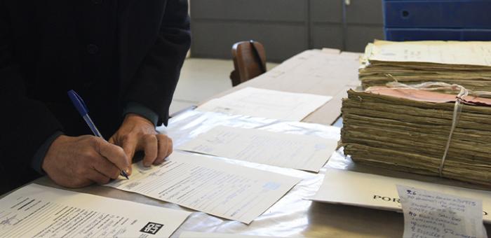 Mano con una lapicera firmando un papel sobre una mesa