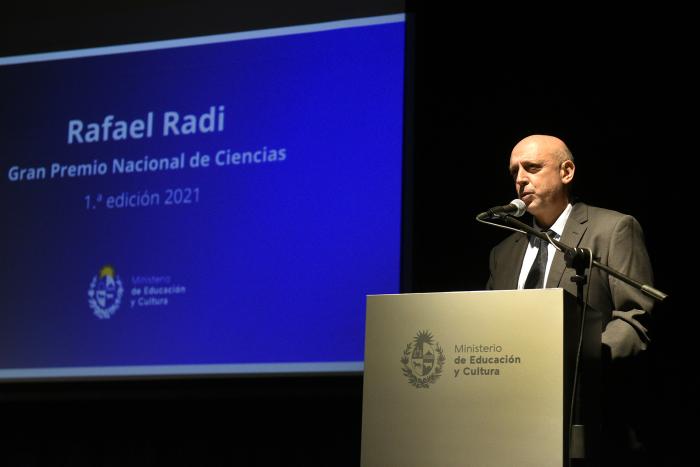 Rafael Radi atrás del atril dando su discurso y a la izquierda se ve una pantalla que dice su nombre