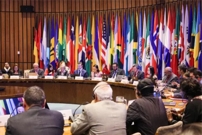 Comité Regional de Educación para América Latina y el Caribe Personas sentadas en una mesa en forma de U con banderas al fondo