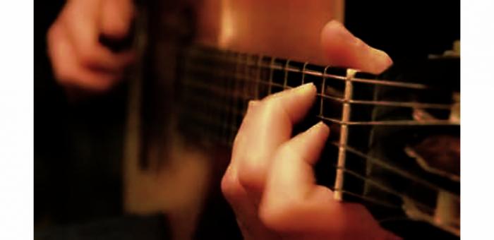 fotografía de guitarra con manos formando acordes
