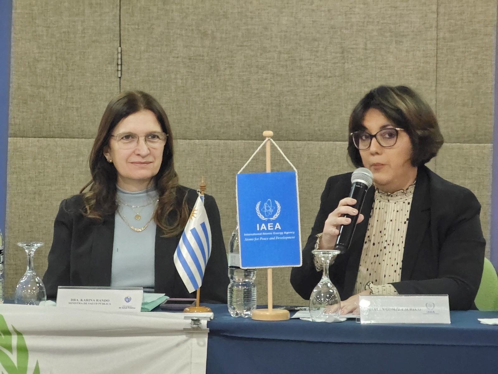 Dos mujeres frente a una mesa. Una de ellas está hablando frente a un micrófono