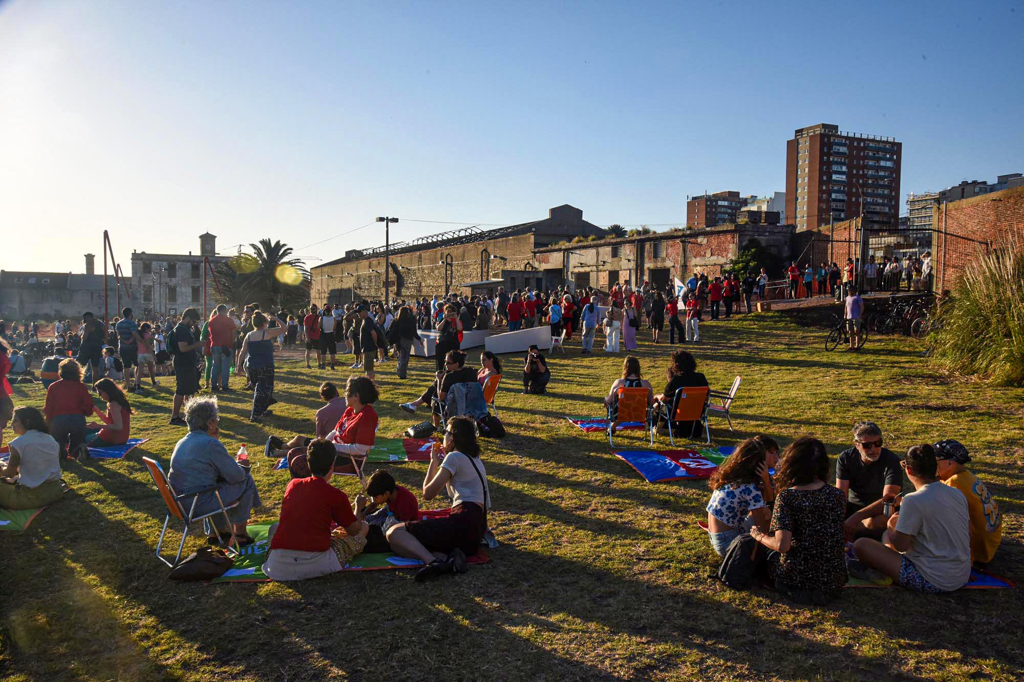 Personas sentadas en el pasto, algunas en reposeras y otras de pie, en el parque