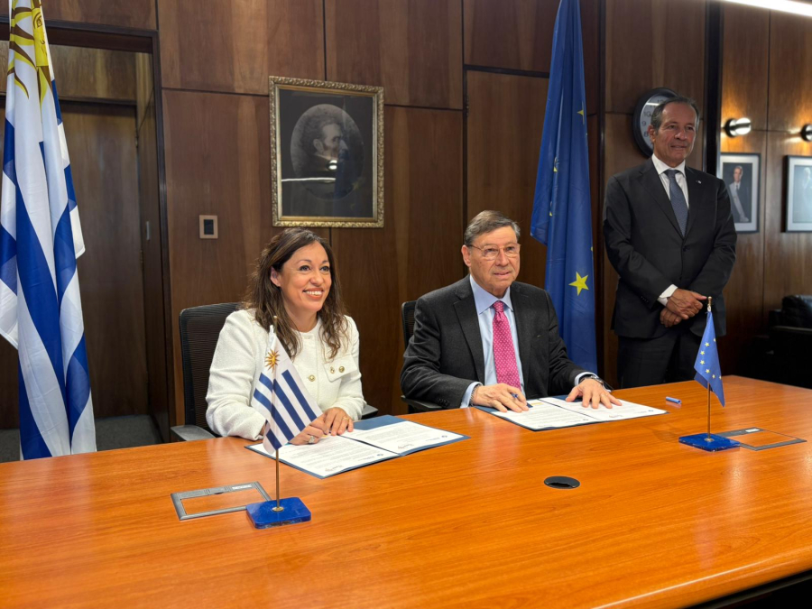 Participantes de la reunión, sentados en mesa y de pie; detrás, bandera