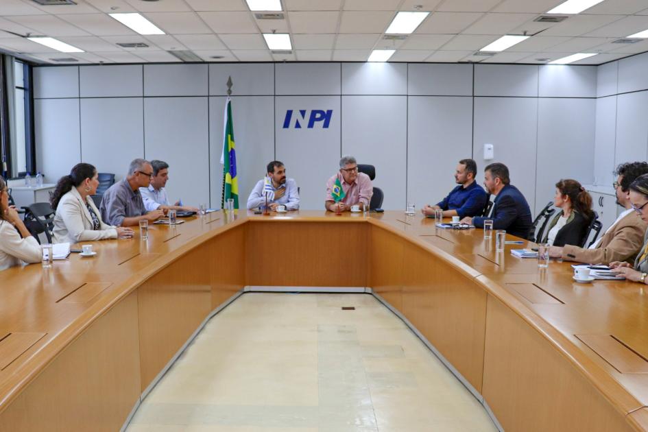 Oficinas de propiedad industrial de Brasil y Uruguay se reunieron en el país vecino Grupo de personas dialogan en una mesa rectangular; al fondo, bandera de Brasil y logo del INPI
