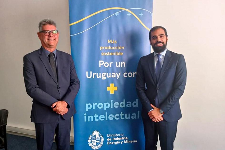 Júlio César Moreira, presidente del INPI, visitó la DNPI; fue recibido por el director Martínez Director Martínez, junto a otro hombre, posan junto a un banner uruguayo