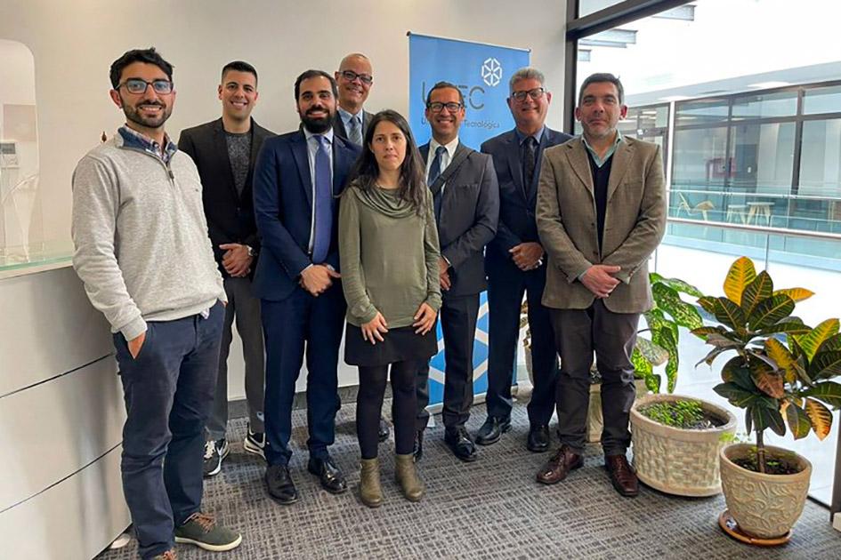 En Uruguay, las delegaciones visitaron la UTEC Grupo de personas posan, de pie, en una oficina vidriada; hay un banner de la UTEC