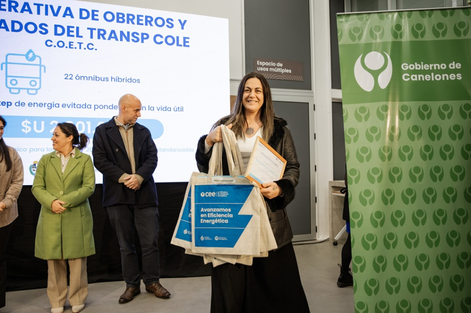 Mujer de frente con bolsas de Certificados de Eficiencia Energética. Detrás, autoridades.