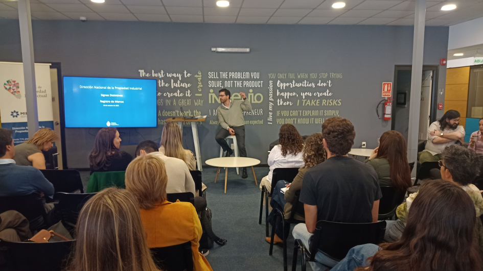 Esc. Bruno Cabrera presentando Marcas. Foto: DNPI Hombre, de pie, realiza una presentación ante el público, sentado
