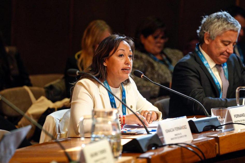 Ministra Fernanda Cardona Ministra Cardona habla en la conferencia, sentada en una mesa con micrófono; a su lado, un hombre