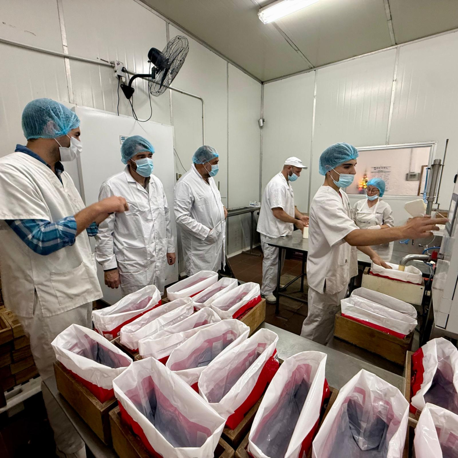 Personas visten túnicas, gorros y tapabocas en planta industrial