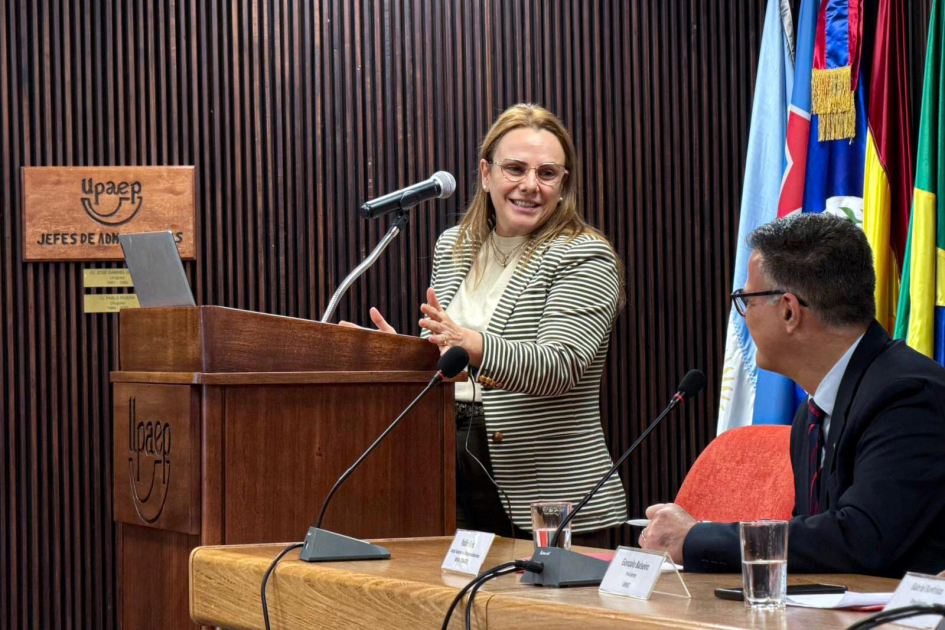 Pérez, de pie tras atril, intercambia sonrisas con Siris, quien se encuentra sentado
