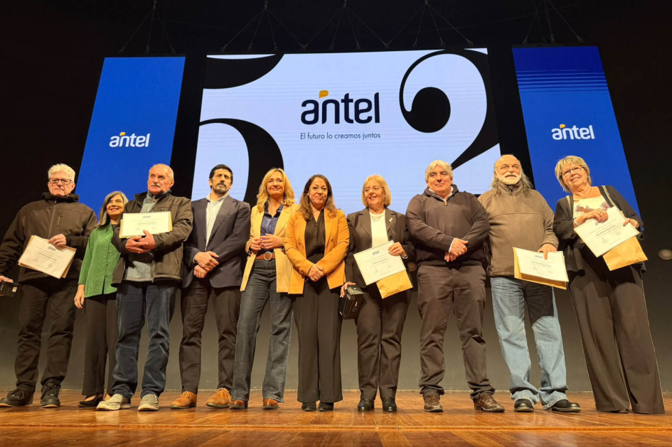 Conmemoración del 52.° aniversario de Antel Autoridades y funcionariado, sobre un escenario; detrás, pantalla