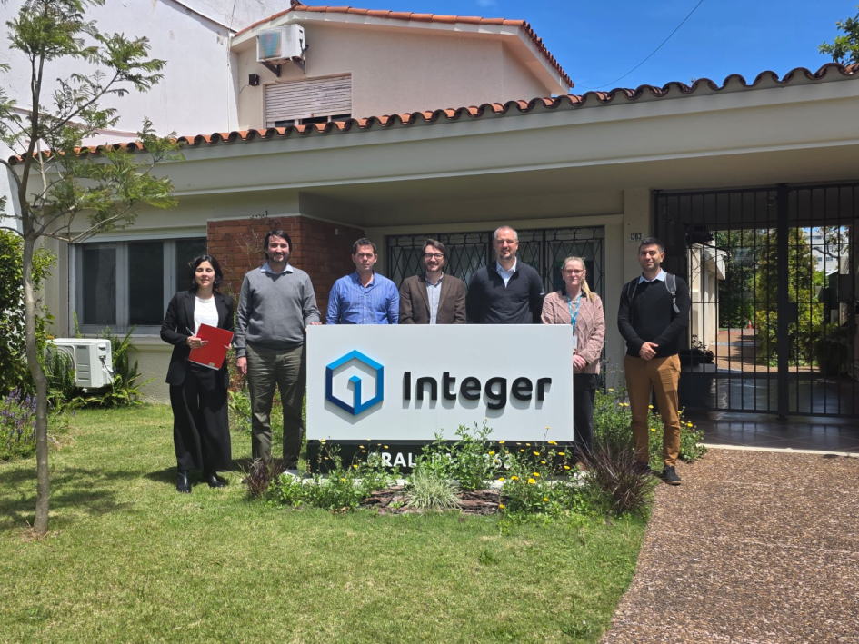 Visita a Integer Personas de pie en un jardín, detrás de un cartel de la empresa