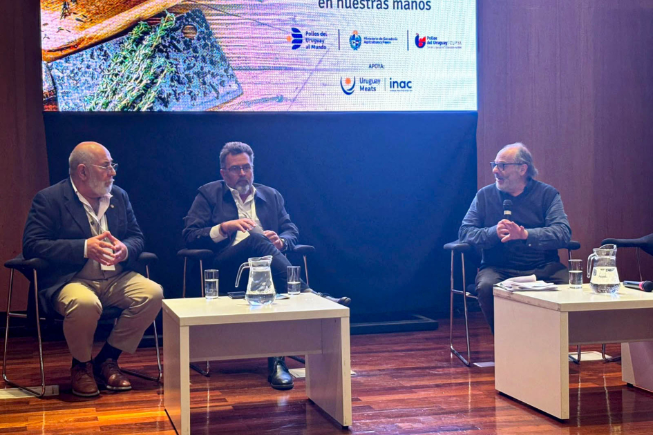 Olesker habla, sentado, junto a Carámbula y Estévez; enfrente, mesas