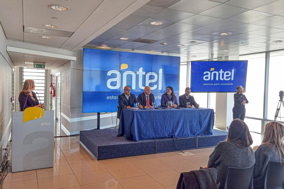 Mesa de autoridades; al frente, público; detrás, un gan banner de Antel; a su lado, un atril