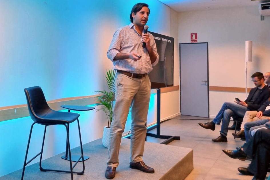 Juan Pablo Tosar, de B4-RNA Un hombre habla sobre un escenario; a sus lados, una silla y una pantalla; enfrente, el público