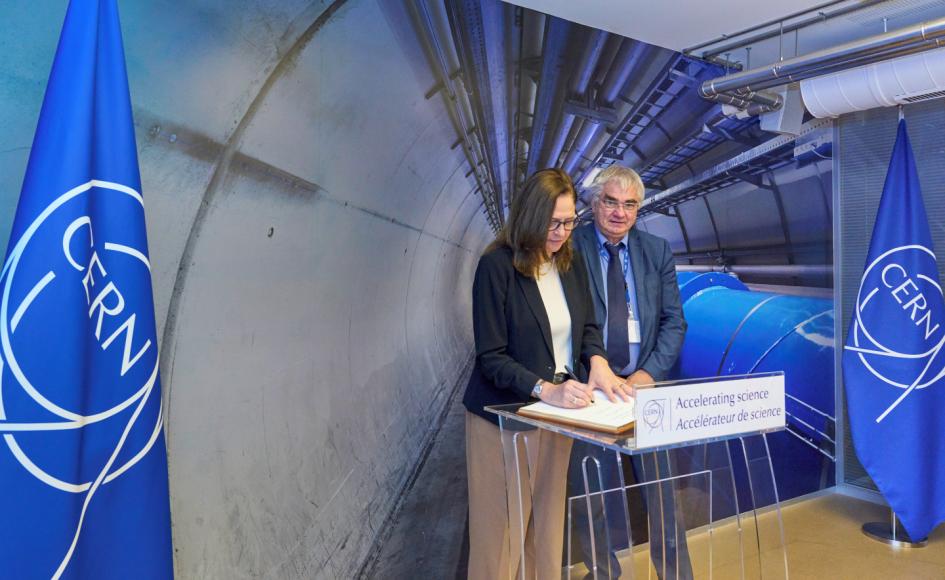 La ministra Elisa Facio representó a Uruguay en la firma del acuerdo de cooperación con el CERN Ministra Facio firma sobre un atril; a su lado, Mnich; detrás, banderas e imágenes del CERN