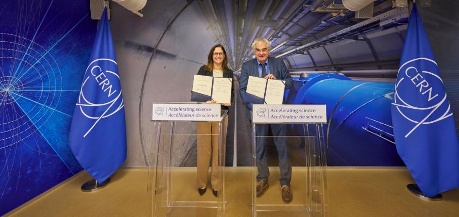 Ministra Elisa Facio y director de Investigación y Computación del CERN, Joachim Mnich Facio y Mnich sostienen los documentos, tras atriles; detrás, imágenes y banderas del CERN