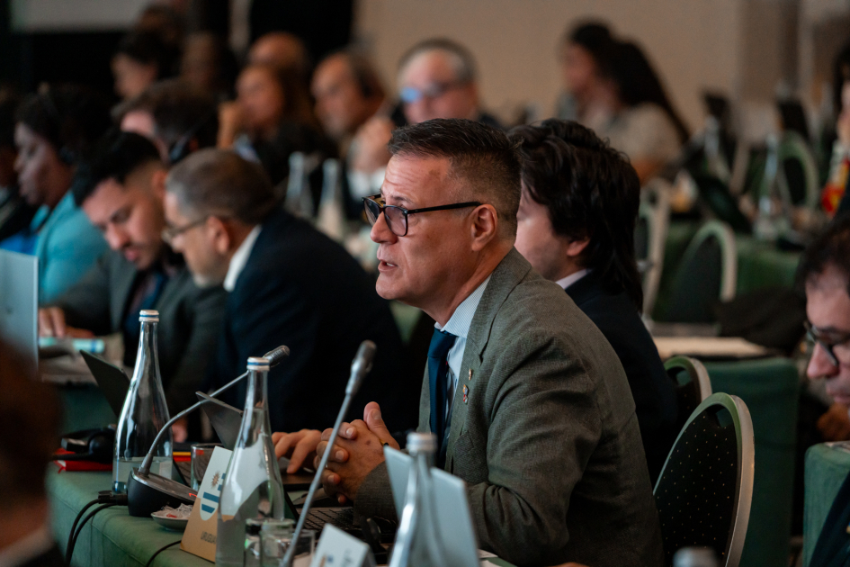 Siris habla, sentado junto a muchas otras personas