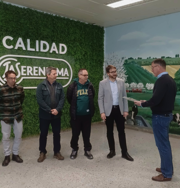 Cinco hombres, de pie; detrás, cartelería de la empresa