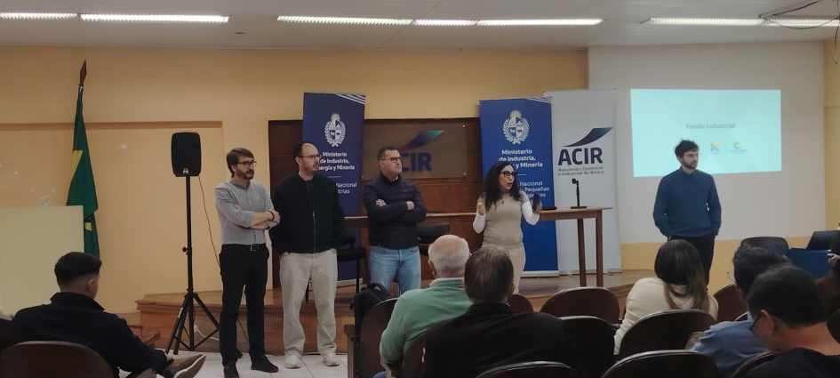 Personas hablan, de pie, ante público sentado