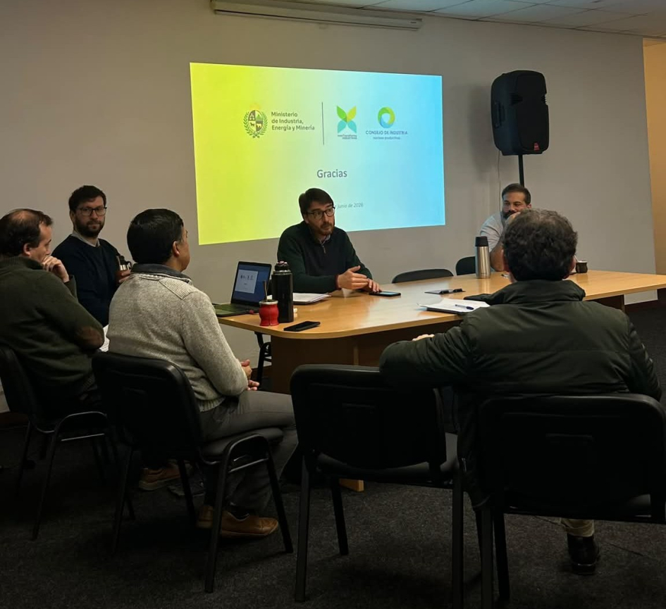 Míguez habla, sentado en una mesa; frente a él, personas; al fondo, diapositiva en la pared