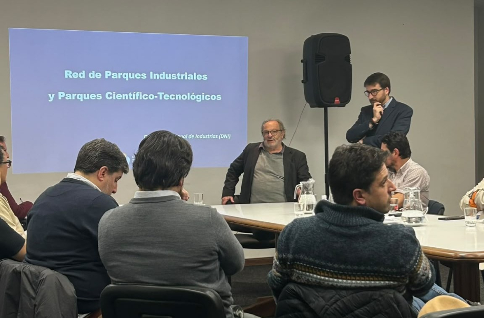Personas sentadas; al fondo, de pie, el director Míguez, y, sentado, el subsecretario Olesker