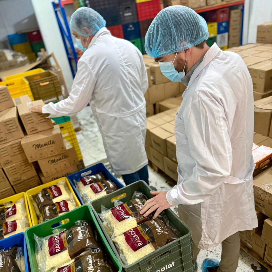 Personas con túnicas, tapabocas y gorros observan queso rallado en planta industrial