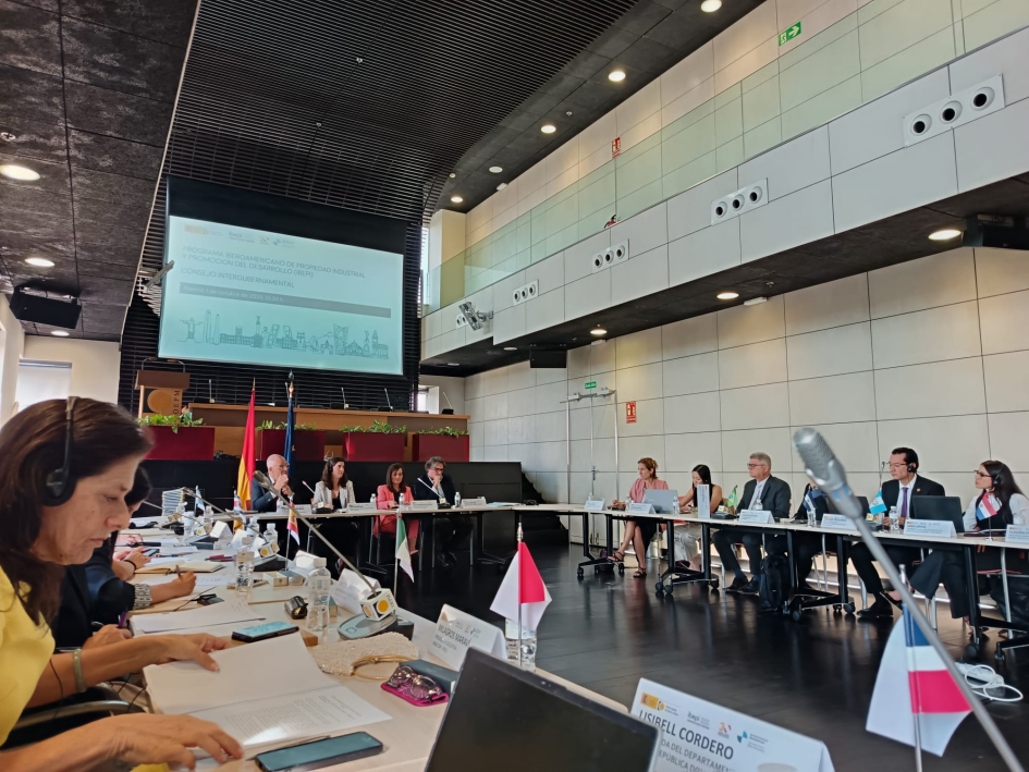 Participantes de la conferencia, sentados y sentadas en mesa de trabajo en forma de "u"