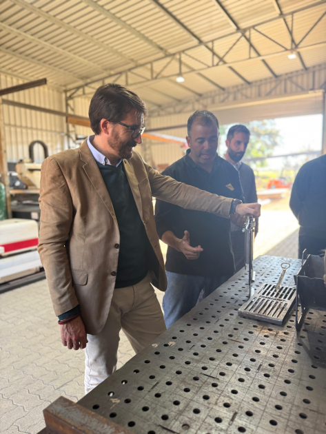 Director nacional de Industrias visitó la empresa Trailersuy Míguez señala un objeto dentro de la planta, junto a otras personas, de pie