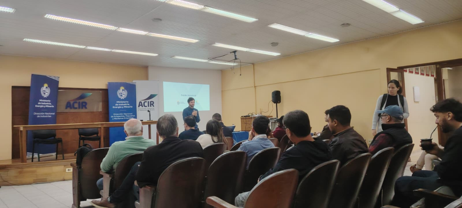 Salón con público sentado; al fondo, personas de pie
