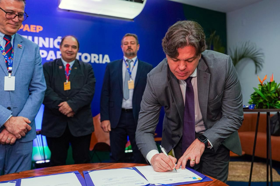 Ministro firma el documento; detrás, otras personas
