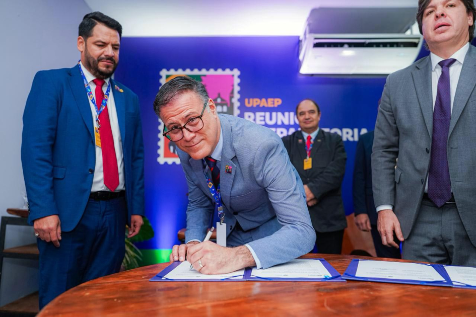 Director Siris sonríe al firmar el documento; a su lado, otras personas