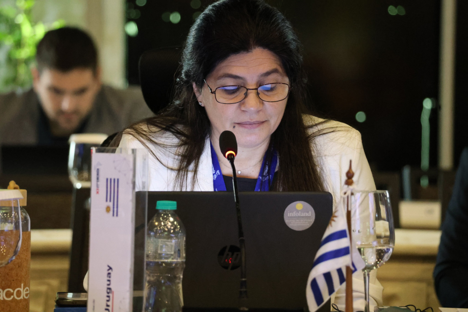 Arianna Spinelli sentada. Frente a ella una laptop y la bandera de Uruguay