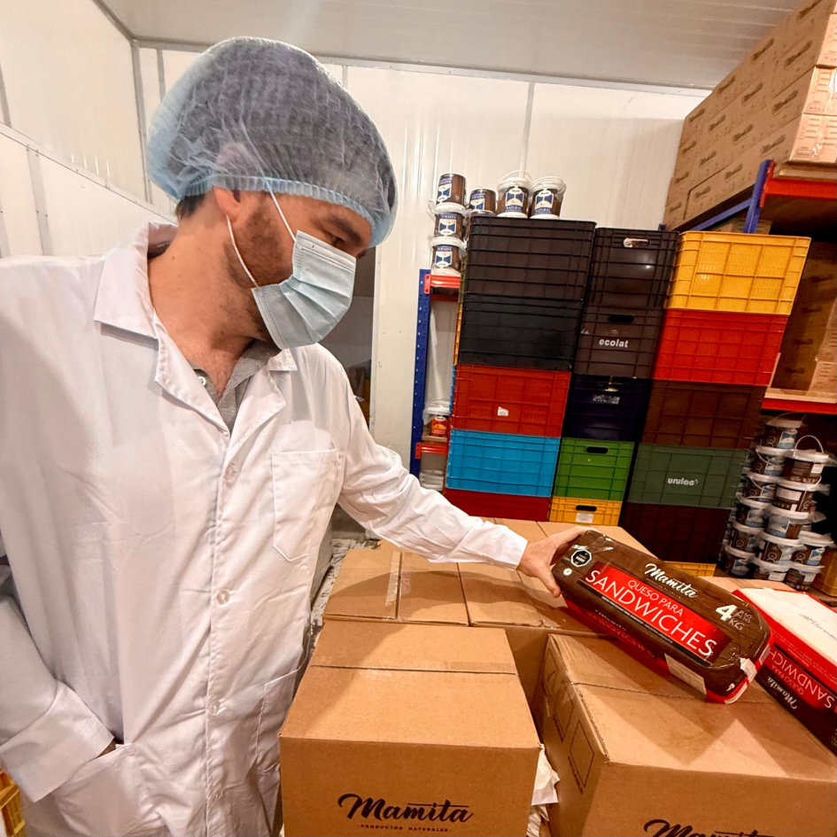 Míguez viste túnica, gorro y tapabocas mientras observa queso de sandwich en planta industrial