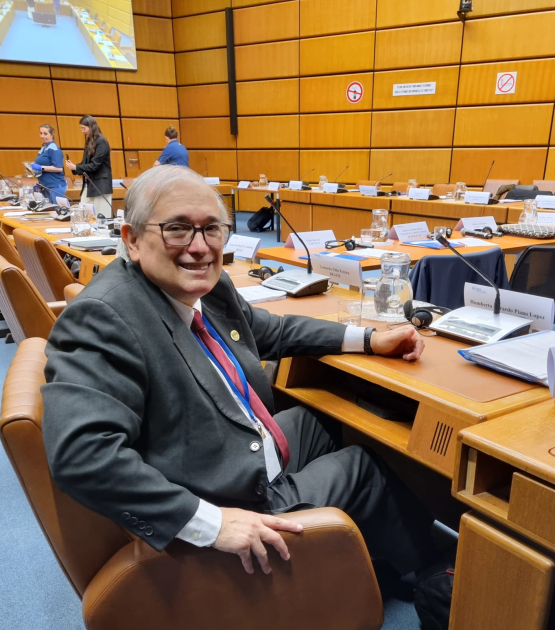 Humberto Piano, sentado en un salón con filas de asientos; hay micrófonos en cada lugar