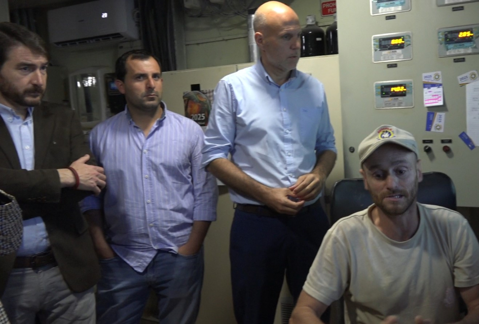 Recorrida en instalaciones de Avícola El Poyote Personas, de pie, junto a un hombre sentado, detrás, una maquinaria