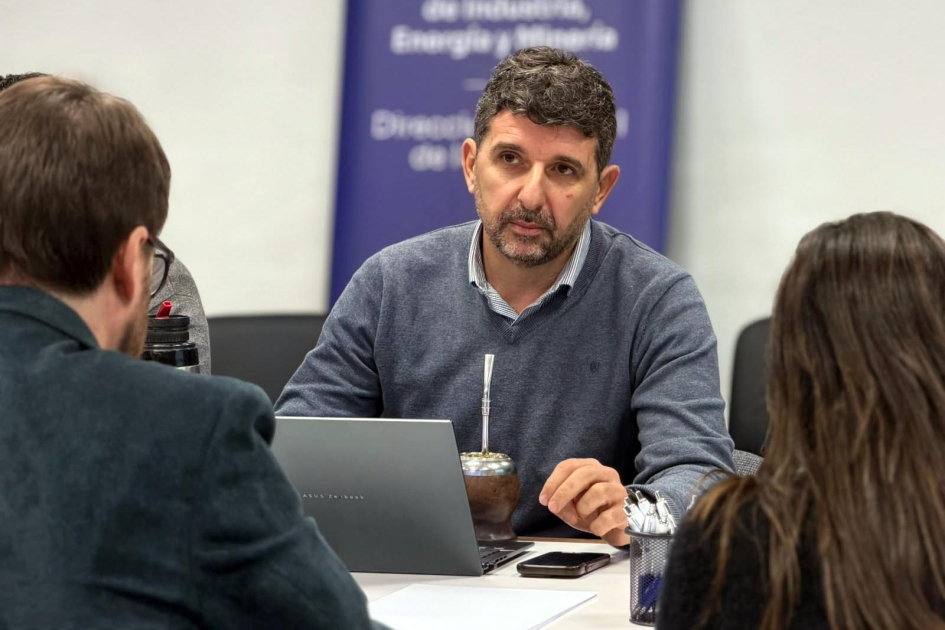 Sebastián Pérez, asesor de la CIU Pérez habla, sentado; frente a él, de espaldas, Cardona y Míguez; al fondo, banner del MIEM
