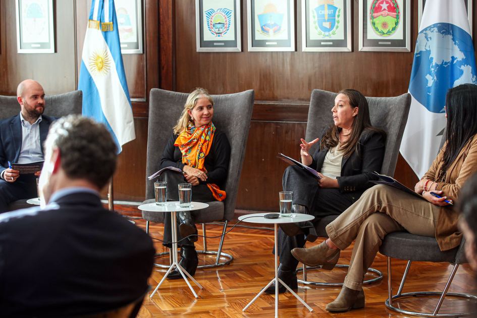 Posente habla, junto a dos hombres y una mujer; de espaldas, escucha un hombre; al fondo, banderas