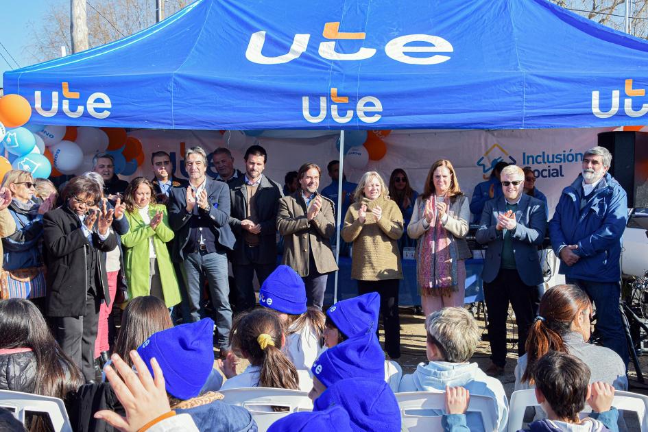 UTE busca alcanzar 12.000 hogares con este plan Autoridades aplauden frente a las familias; arriba, toldo con logo de UTE