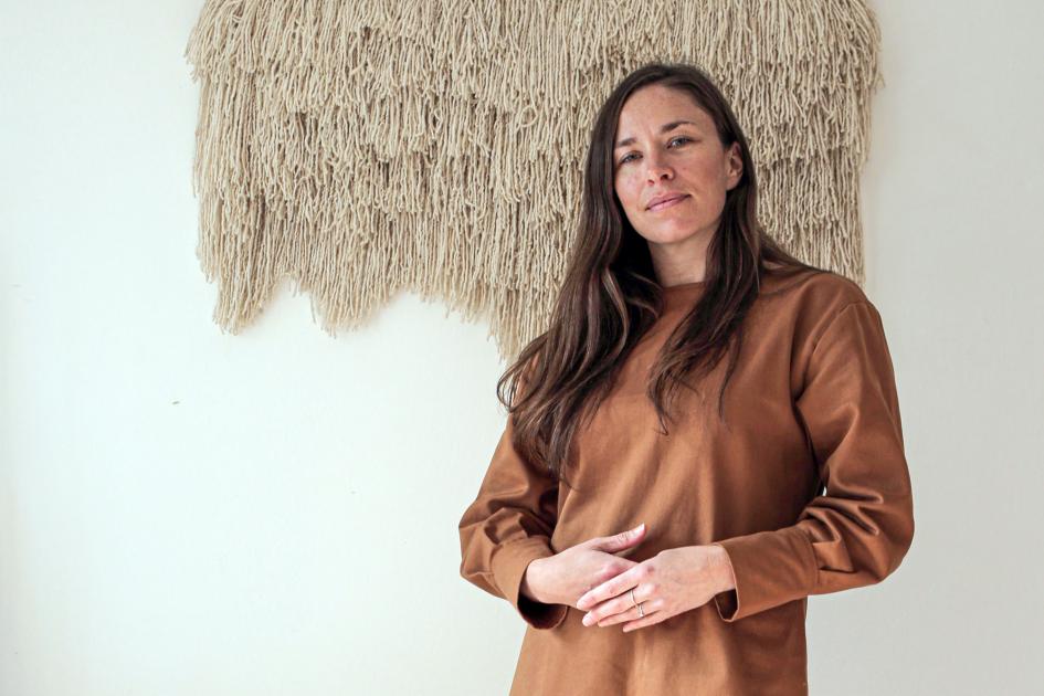 Claudia Rosillo, de Texturable Se ve a Claudia y detrás, sobre una pared, un producto tejido de su empresa