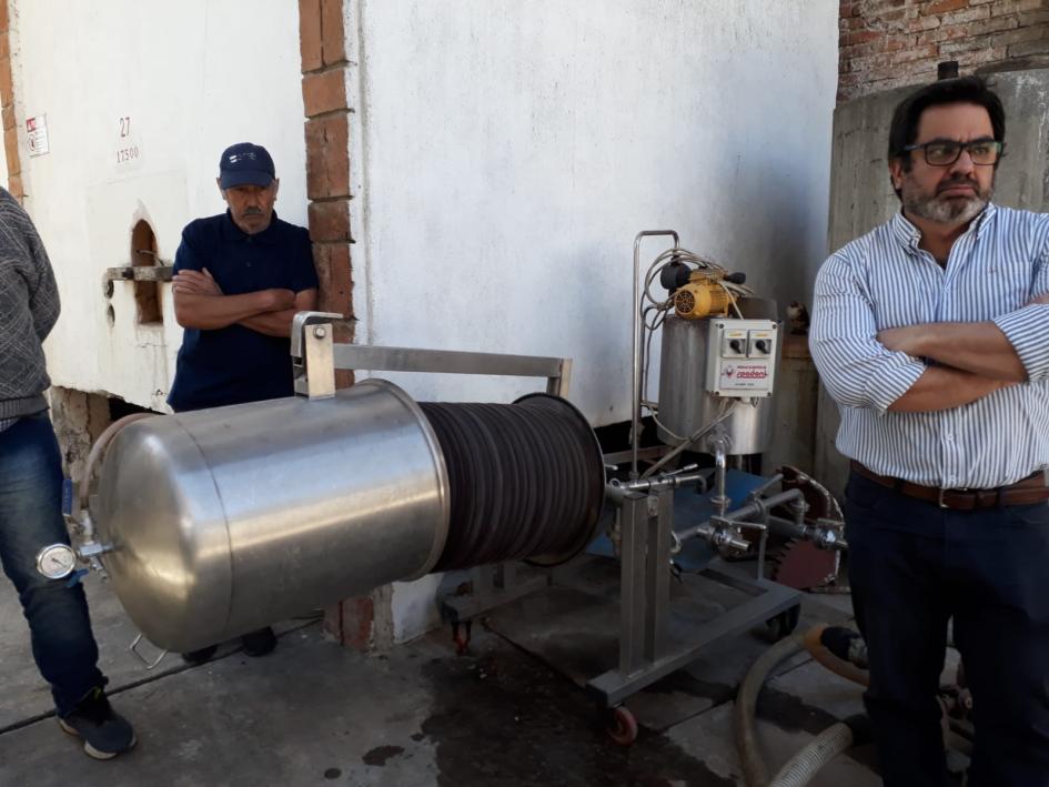 Maciel está dentro de una planta, en la que se ven dos personas (una de ellas, a cuerpo compleeto)