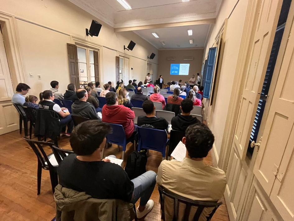 Participantes en el curso Inocuidad y buenas prácticas en la elaboración de alimentos Personas sentadas en sillas; al fondo, una pan talla
