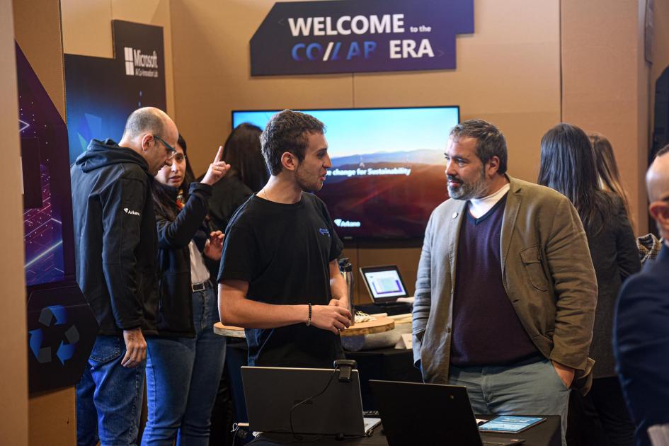 Parte de la exposición de emprendimientos acelerados Personas dialogan en la exposición; hay una pantalla