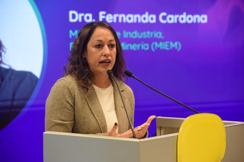 Cardona habla desde un atril; detrás se ve fragmento de pantalla con su nombre y cargo