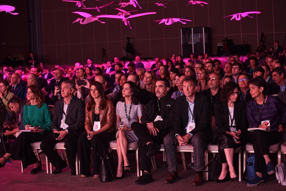 Público en la gran sala del centro de convenciones, con luces rosadas