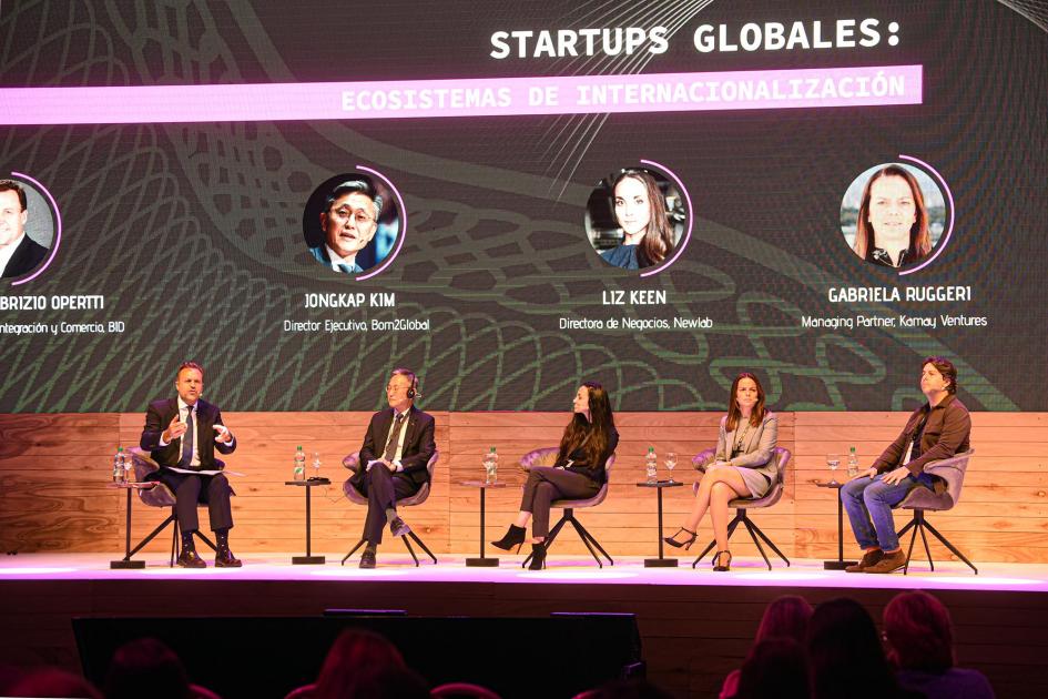 Panel sobre startups globales Tres hombres y dos mujeres están sentados en sillas individuales sobre el escenario