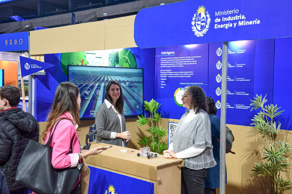 Stand del MIEM Personas interactúan en el stand del MIEM, donde predomina el azul y hay pantas